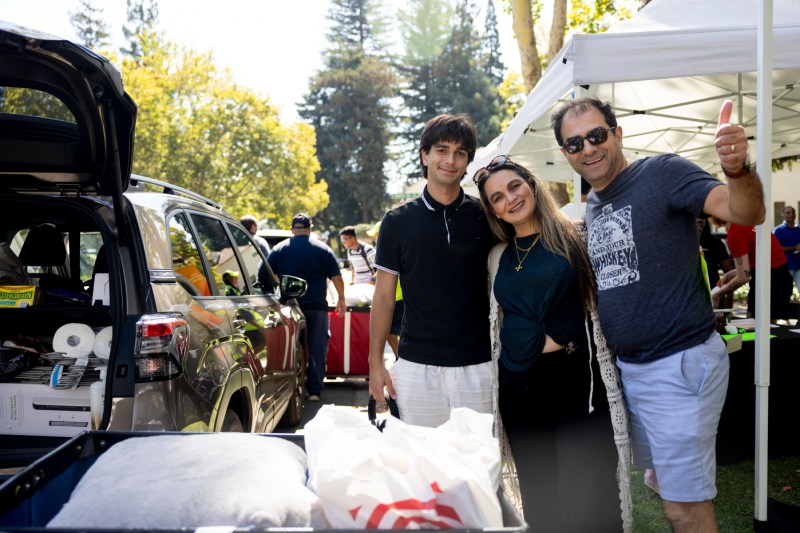 A family poses for a photo near a car as they unload their move-in supplies. 