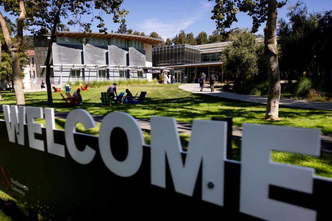 A view of Northeastern’s Oakland campus with students walking and sitting on the lawn near a “WELCOME” sign and outdoor seating.