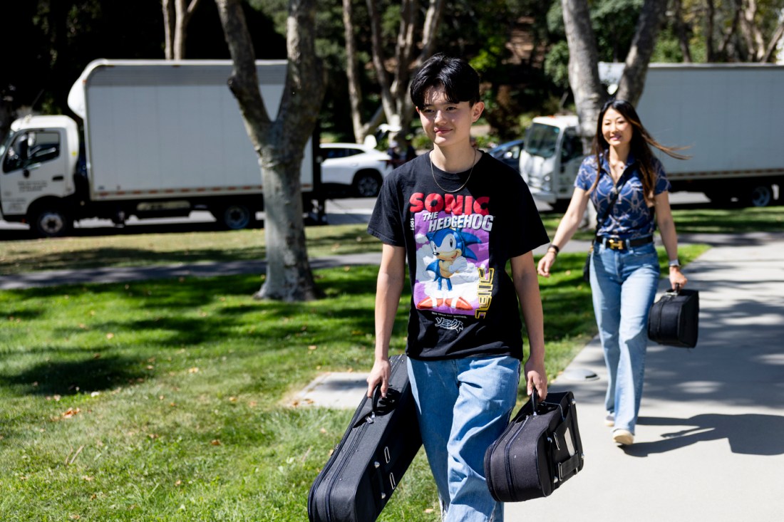 Two Northeastern students walk through campus carrying boxes on move-in day during Fall Orientation Week.