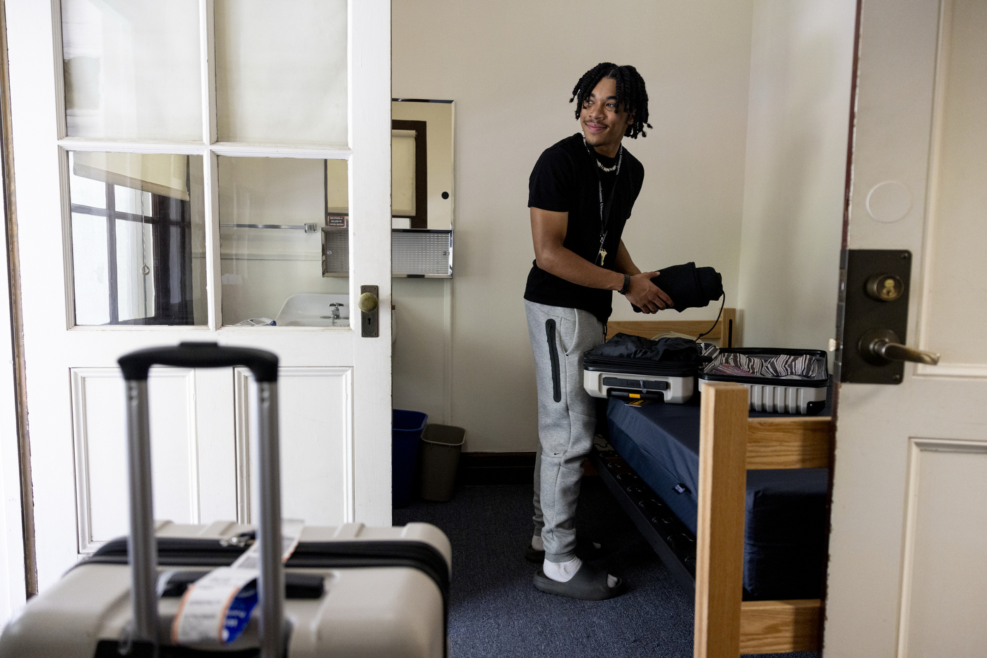 A student smiles as they unpack their suitcase in their new dorm room
