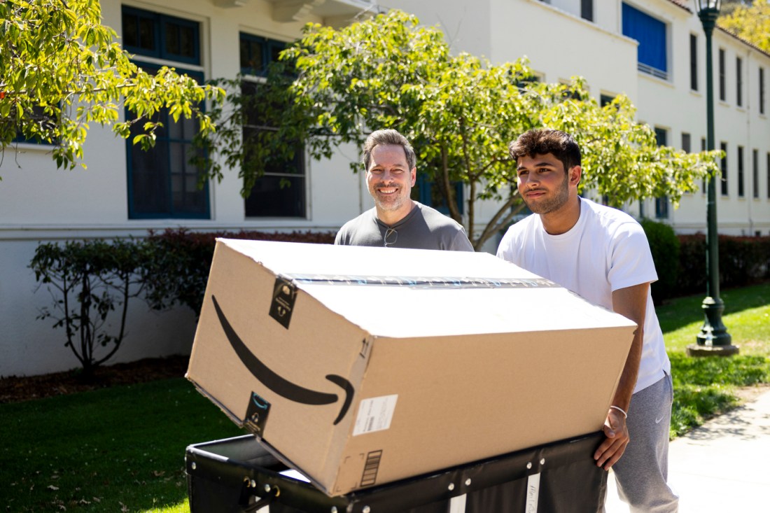 A Northeastern student and another man shown smiling and carrying an Amazon package during Welcome Week.