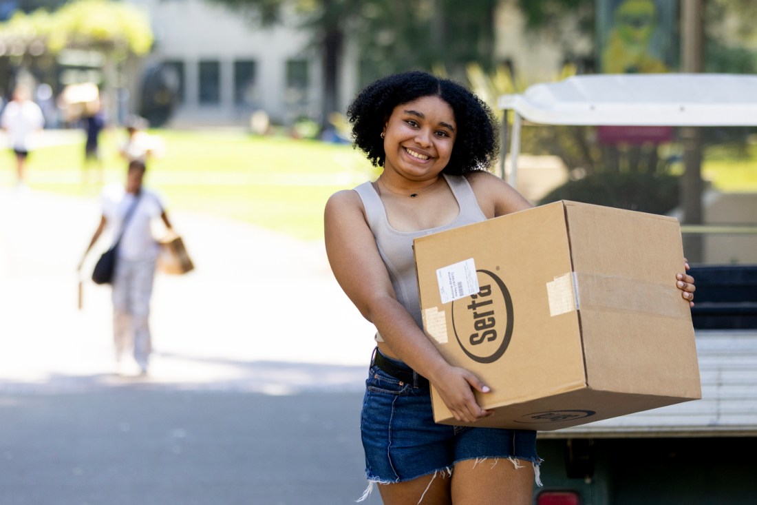 A Northeastern student smiles while carrying boxes across the Oakland campus on move-in day.