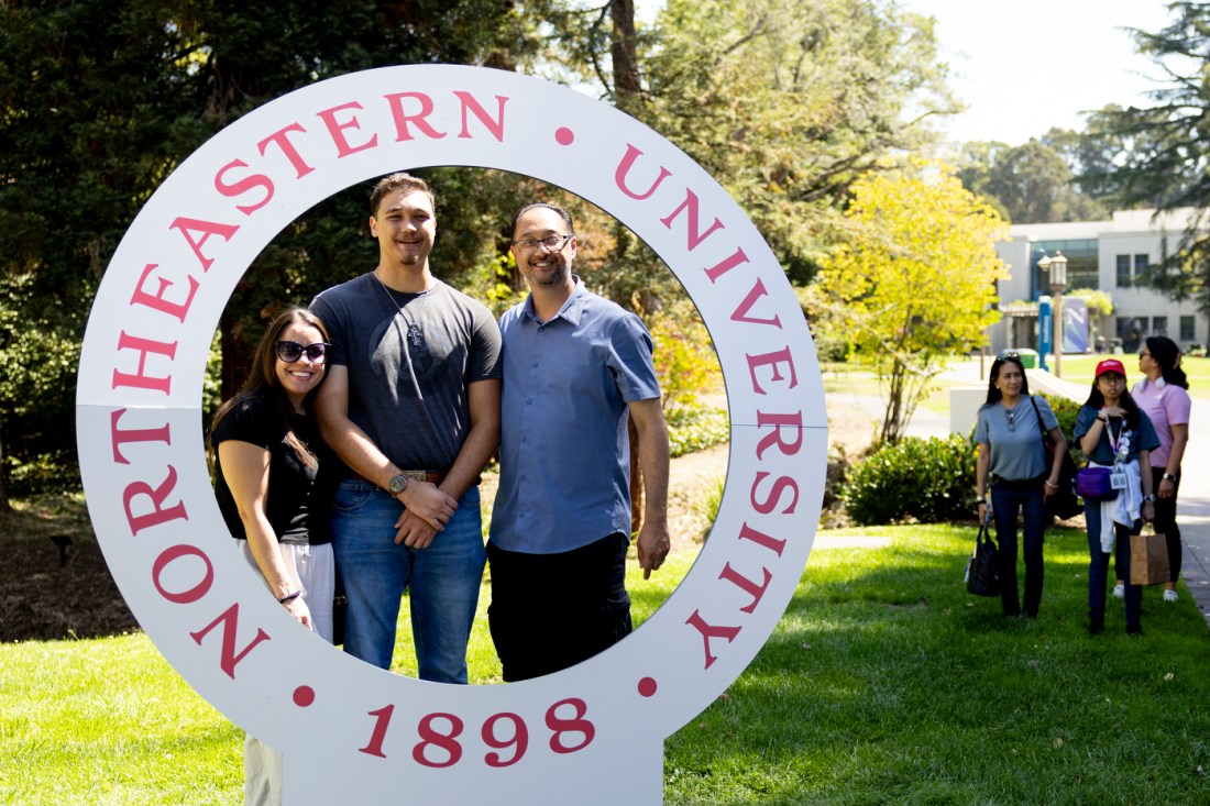 Two people stand under a larch white circular photo prop that says 'NORTHEASTERN UNIVERSITY' on it in red letters. 