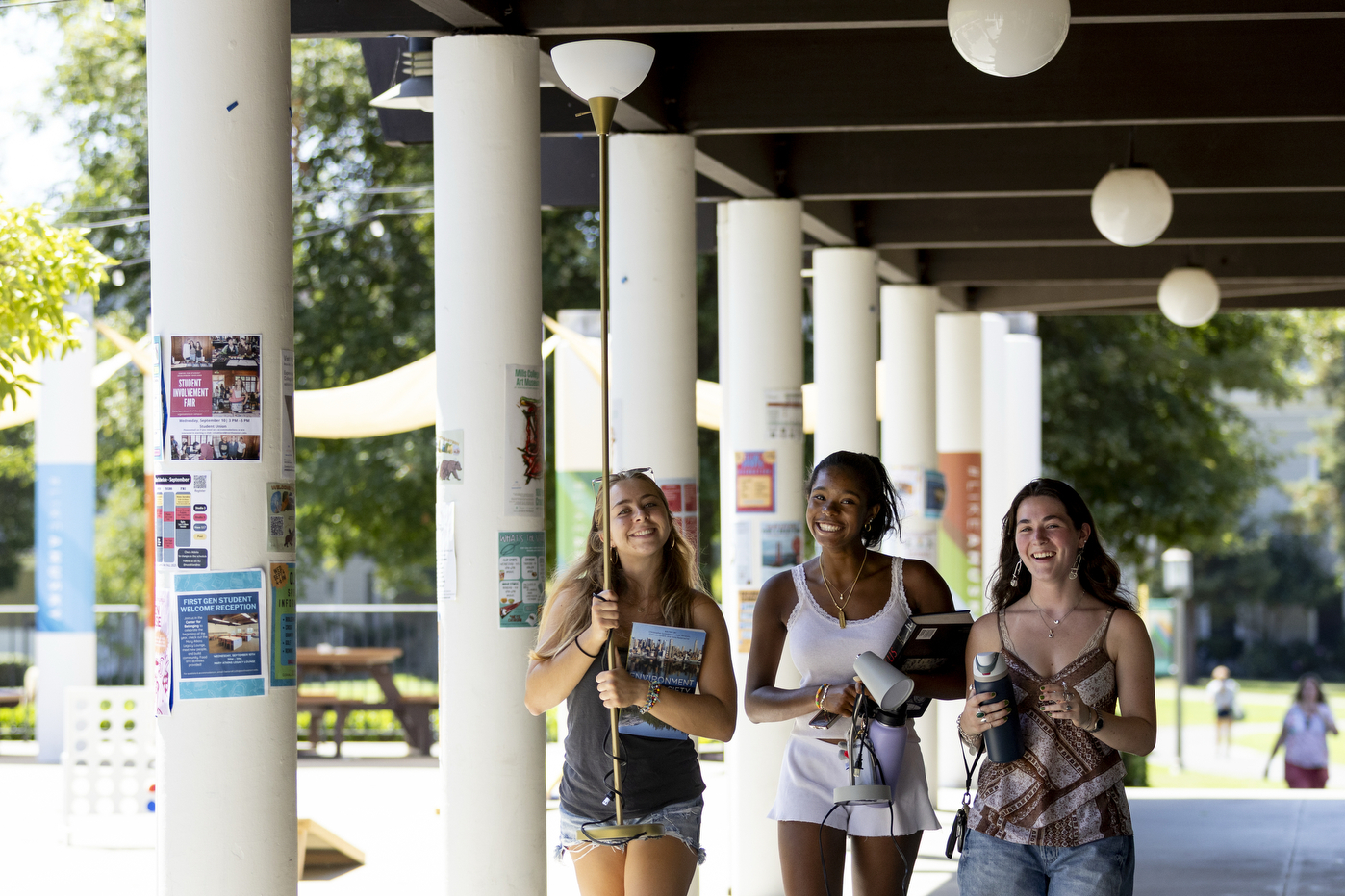 Three students carrying move-in supplies smile for a photo on the Oakland campus.