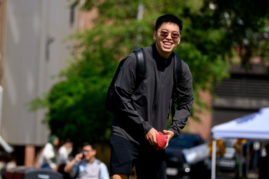 A student wearing a long sleeved black jacket smiling while holding a red beanbag.