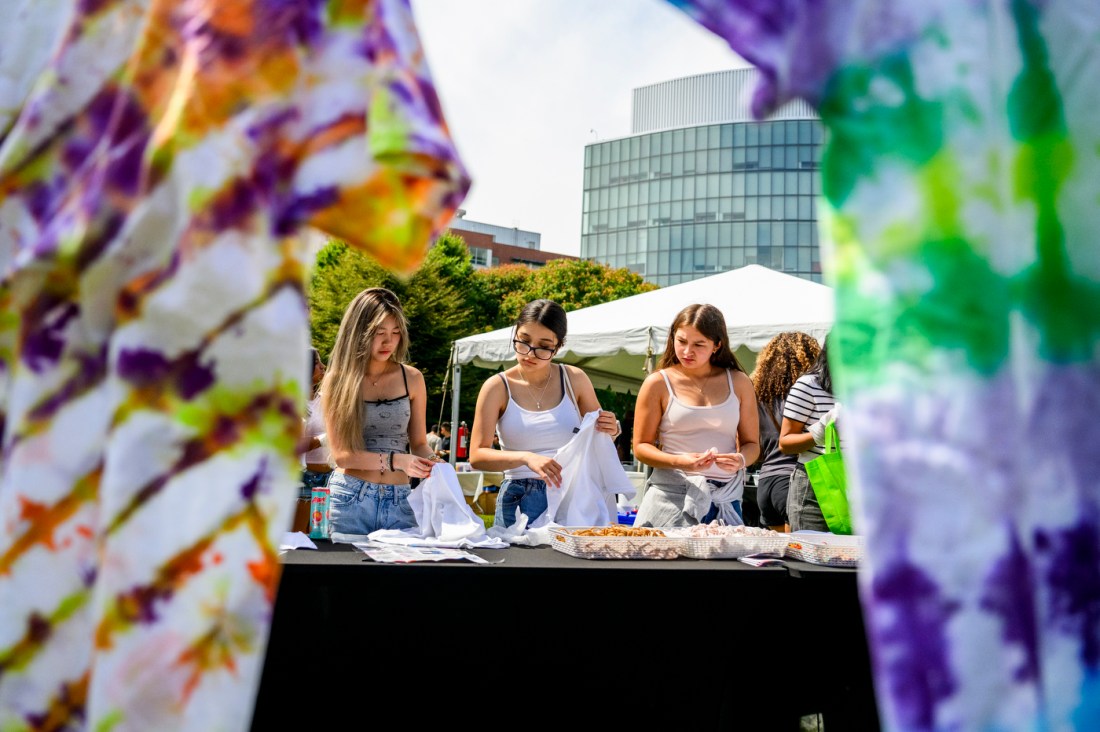 Three students standing at a table holding white t-shirts for tie dye.