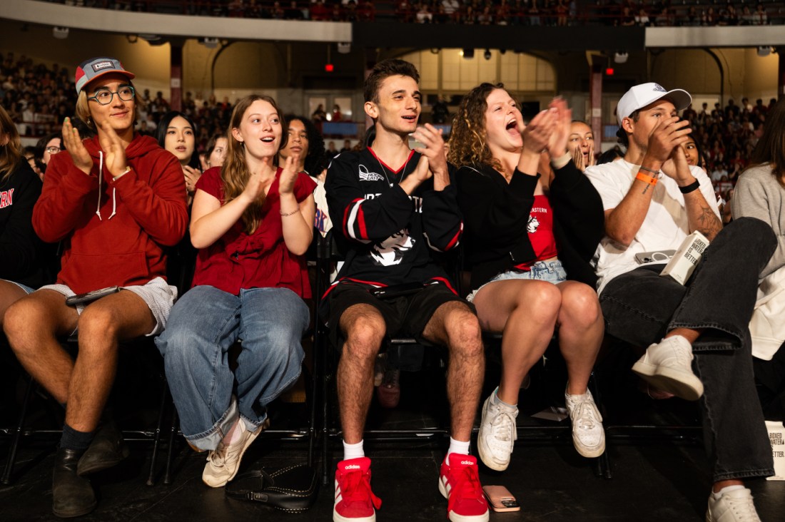 A group of students in the arena clap and cheer enthusiastically during convocation.