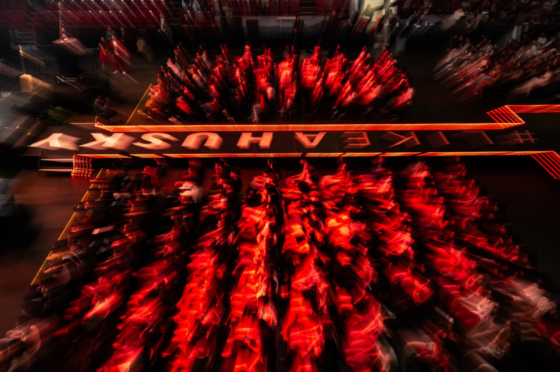 A wide shot of the arena floor filled with students in red light, with “HUSKY” projected boldly across the scene.