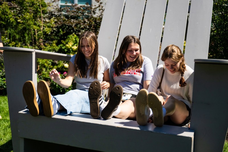 Three students sit in a giant Adirondack chair. 