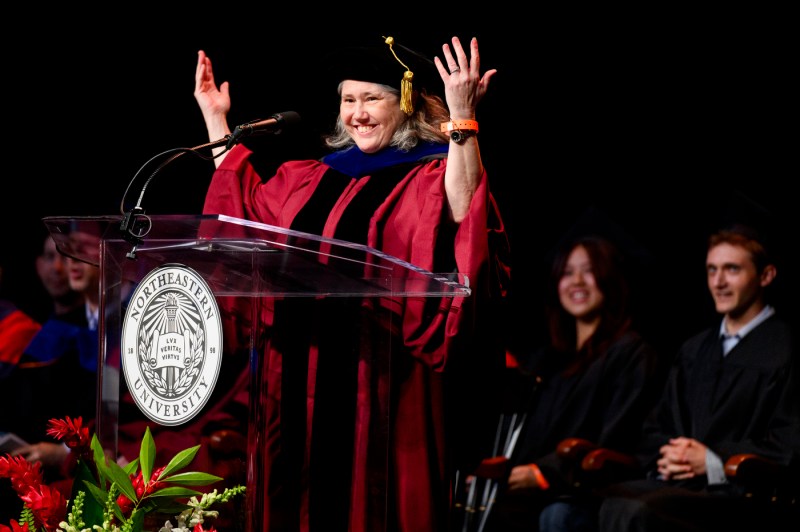 Beth Winkelstein stands in front of a podium with her hands raised at convocation.