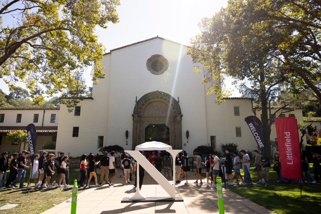Students line up outside Littlefield Concert Hall beneath trees and sunlight on the Oakland campus.