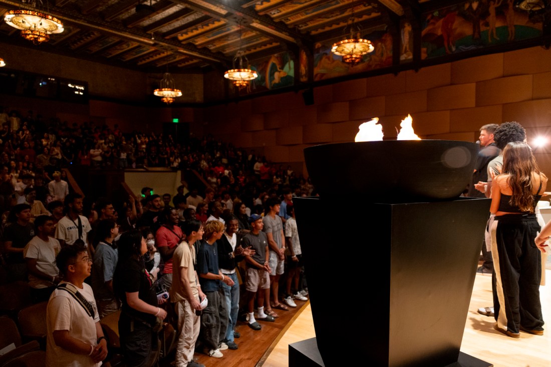 Students stand onstage around the ceremonial torch inside Littlefield Concert Hall during Northeastern’s Oakland welcome event.