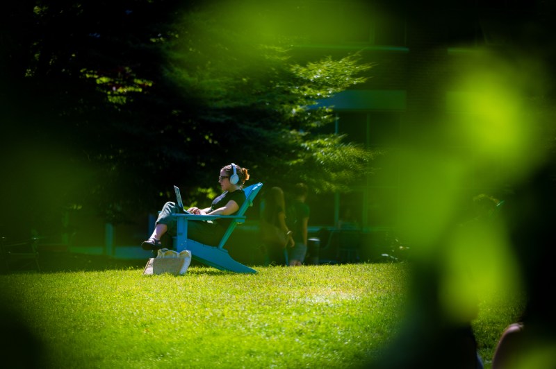 A student sits in an Adirondack chair while on their laptop.