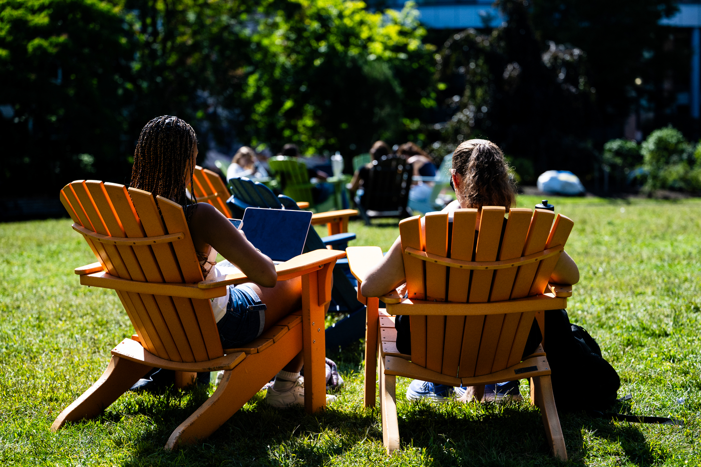Two students sit in Adirondack chairs while working.