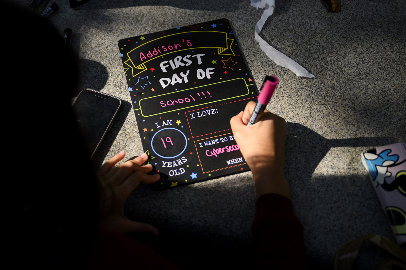 A student fills out a "First Day of School" blackboard with their name and age.