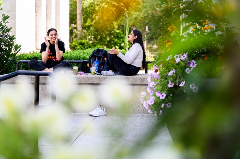 Students sit outside on a step on the Boston campus.