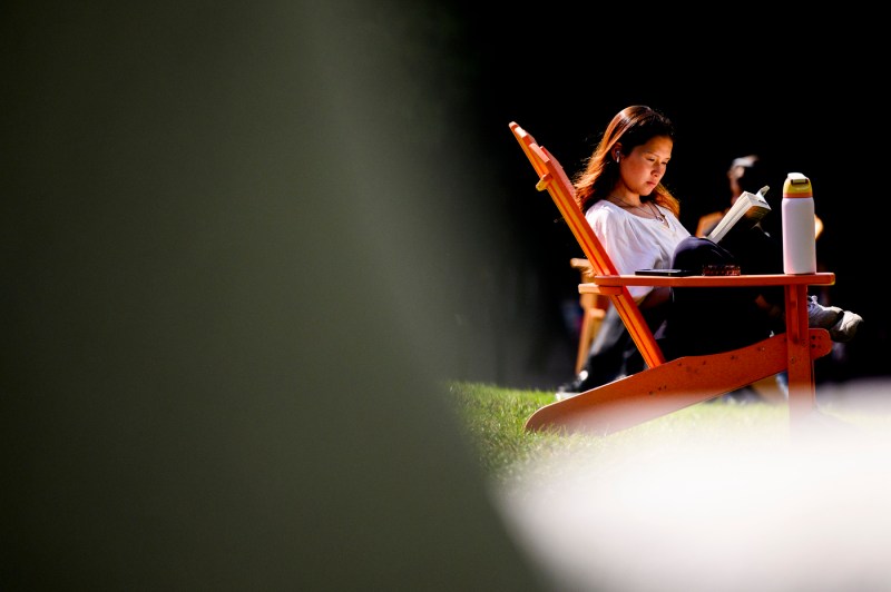 A student sits in an Adirondack chair while reading. 