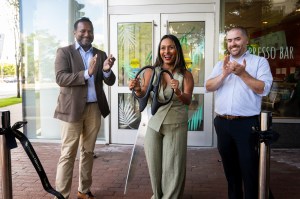 Ammy Lowney shown cutting the ribbon alongside a man in a tan suit and another man with a striped shirt.