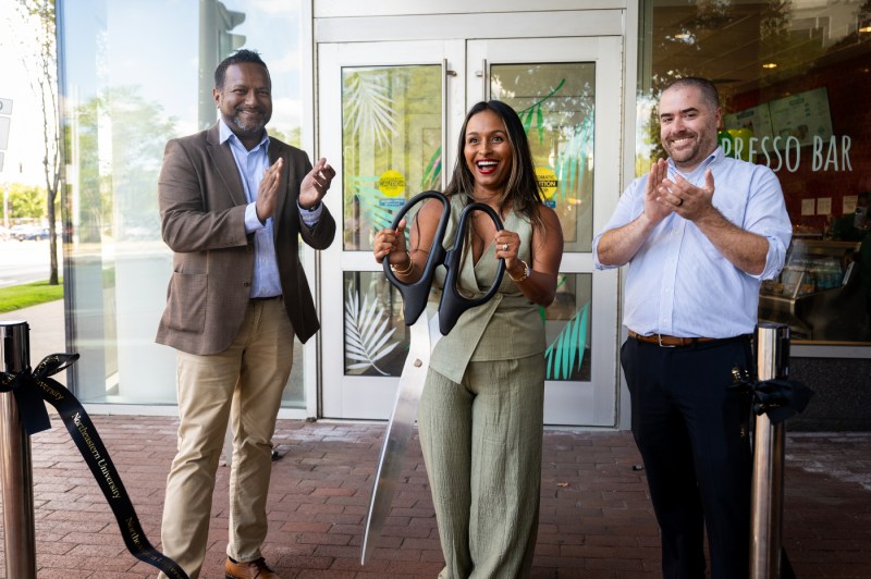 Ammy Lowney shown cutting the ribbon alongside a man in a tan suit and another man with a striped shirt.