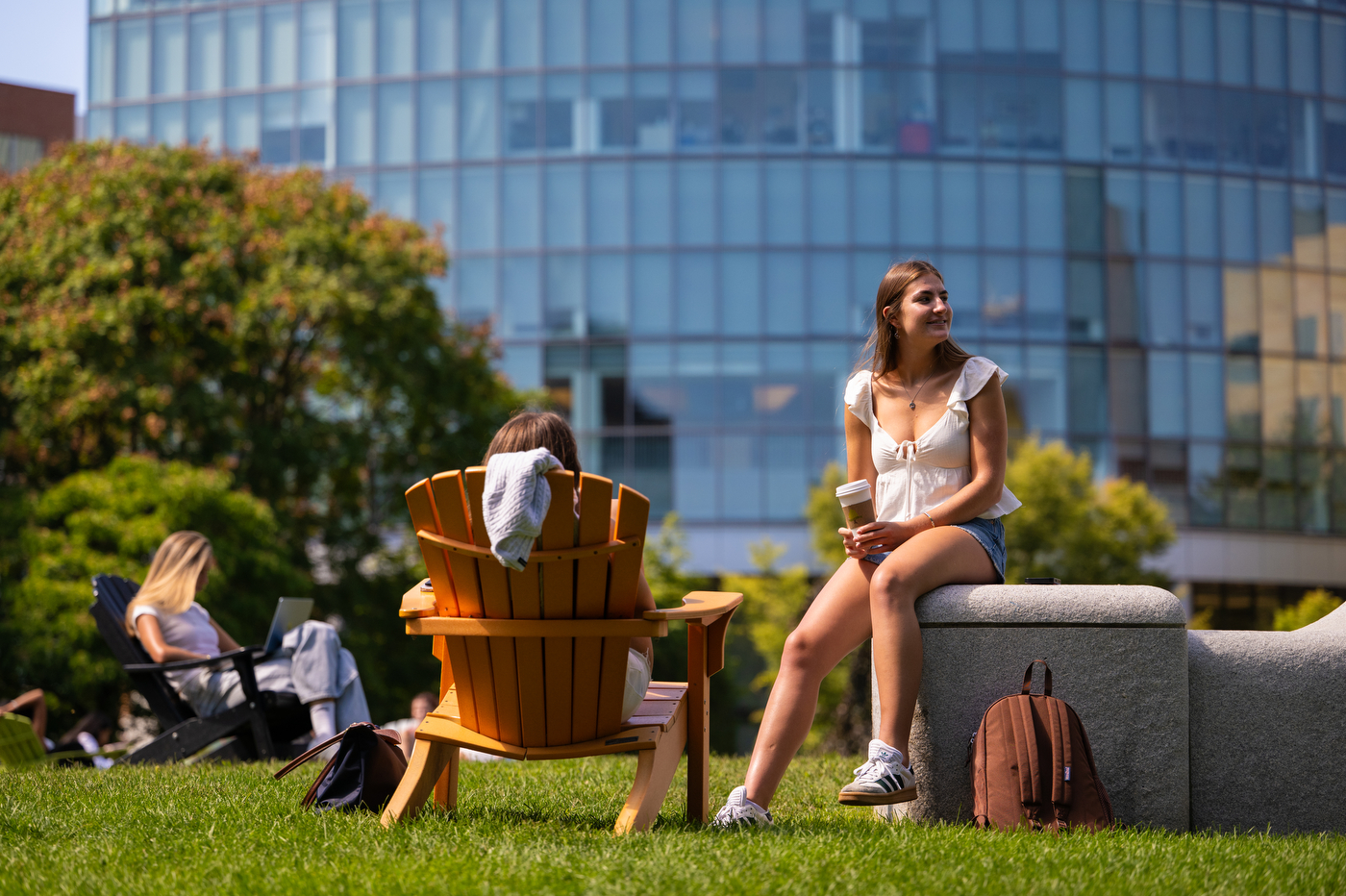 A student sits in an Adirondack chair while another sits on a stone wall.