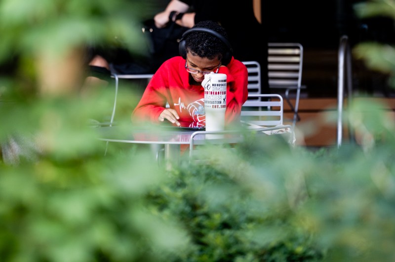 A student sits at a table outside.