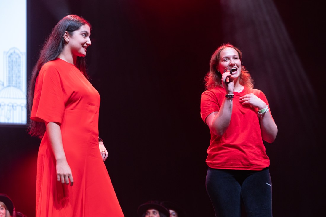 Two speakers, one in a red dress, another in a red shirt, address the audience during Convocation.