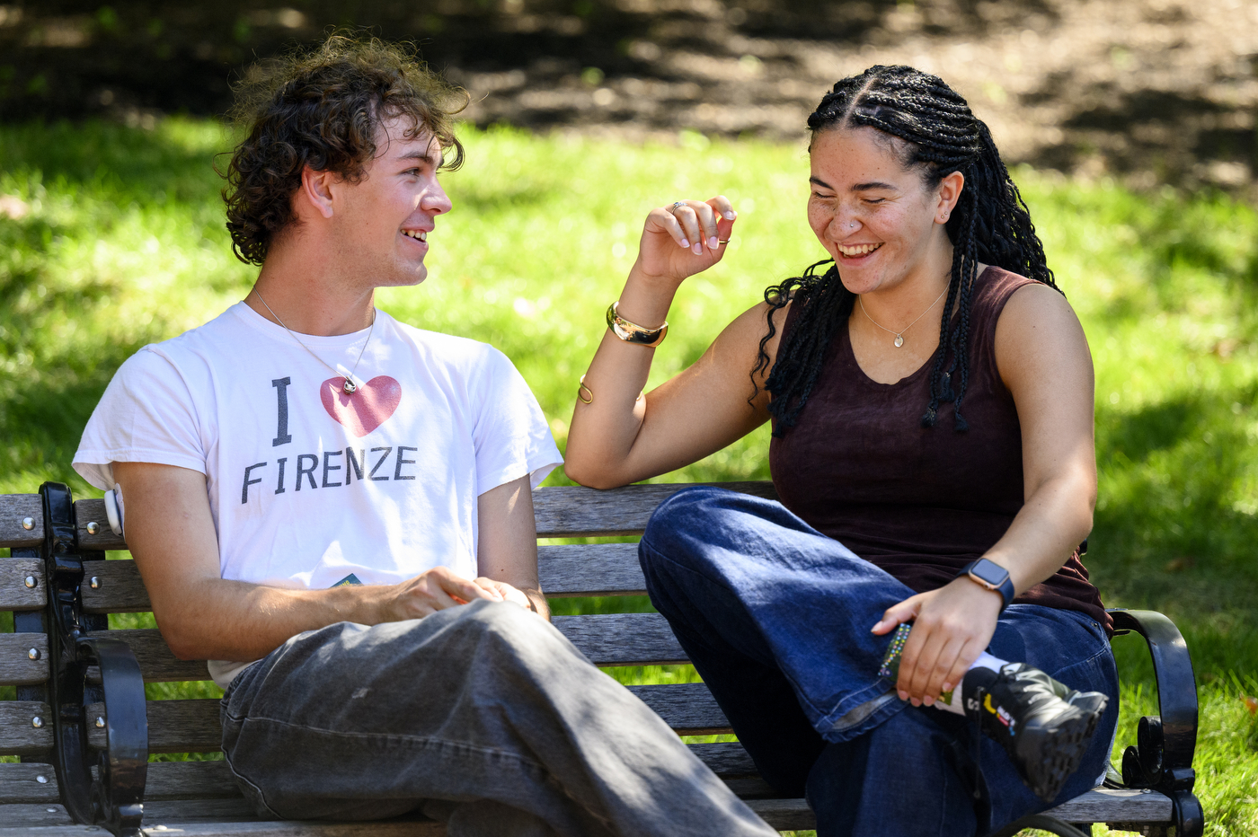 Two students sit on a bench outside while chatting.