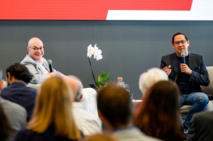 President Aoun wearing a grey suit and Spencer Fung wearing a black suit both sitting on a raised stage holding microphones. In between them is a white orchid flower.