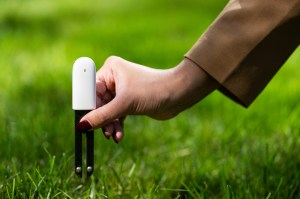 The arm of a person holding a smart irrigation device to the grass.