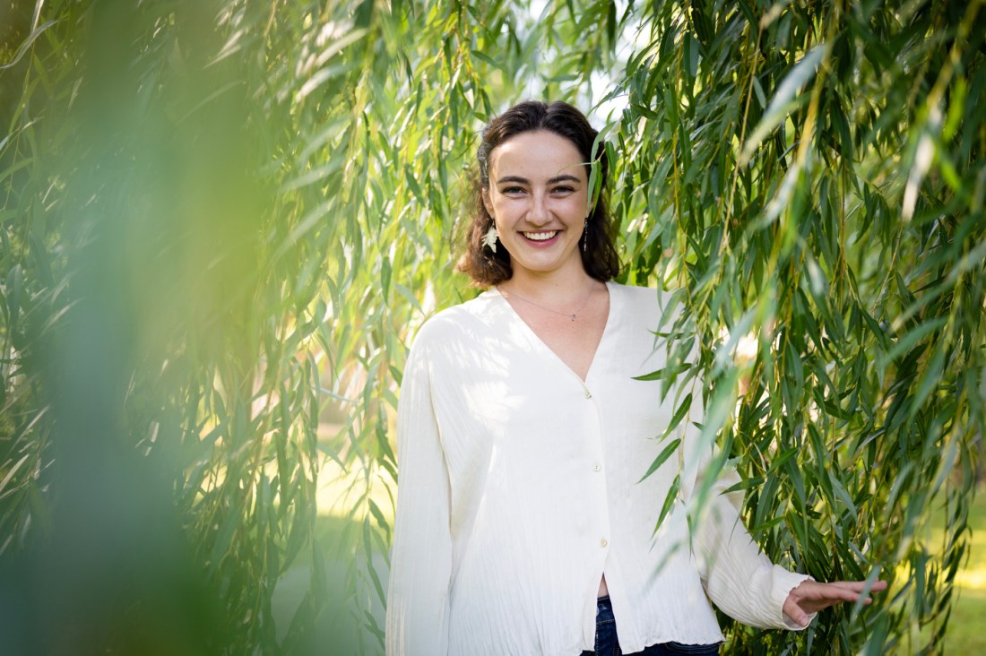 Isabelle Wood smiling in a white shirt as she stands between stalks of tall grass.