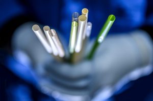 A collection of various drinking straws in a researcher's gloved hand in a laboratory setting.
