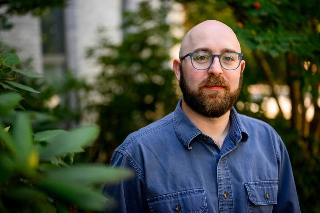 Portrait of Bryan James standin goutside wearing a blue denim button down and glasses. 