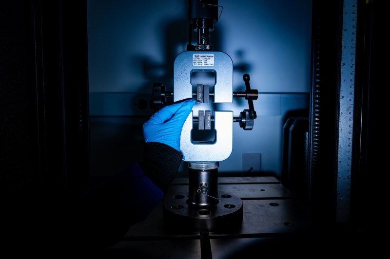 Laboratory testing machine with gloved hands preparing equipment for bone research experiment.