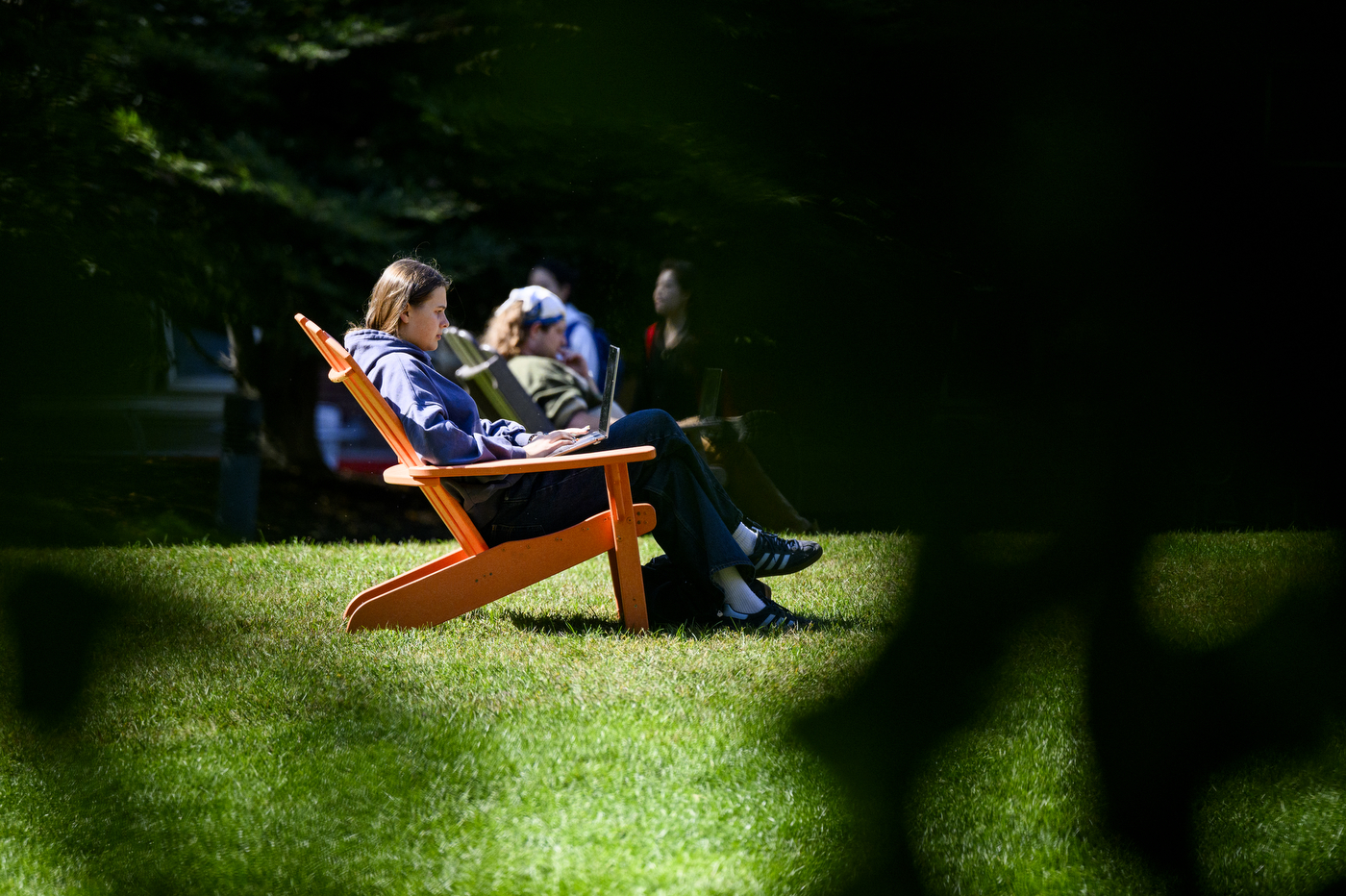 Students sit on colorful Adirondack chairs on a lawn.