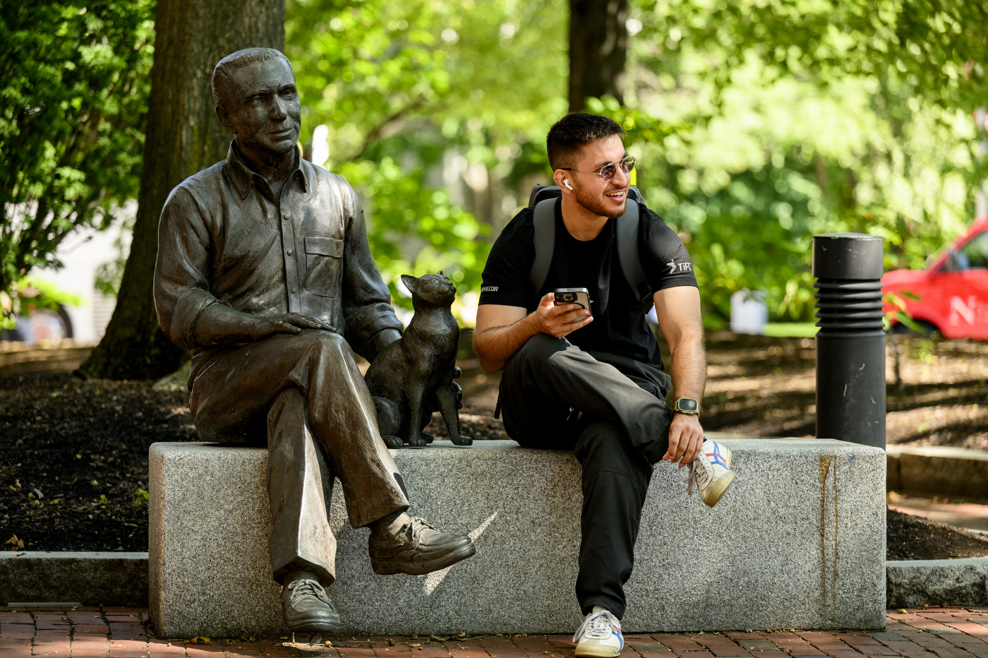 A person sits on a stone bench next to a statue of a person and a cat.