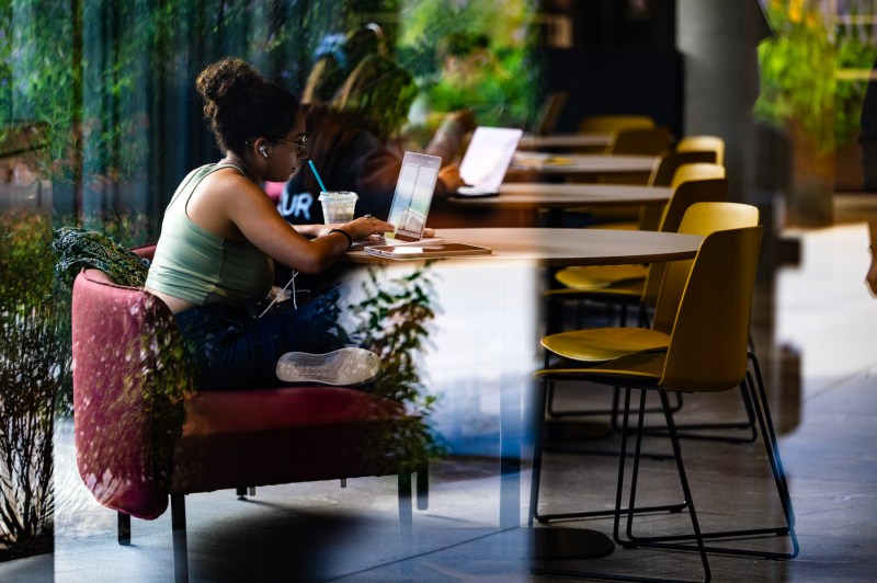 Students sit at circular tables while working on laptops and sipping coffee.
