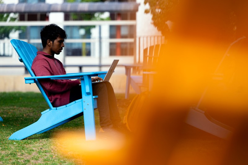 A student sits on an Adirondack chair while working on their laptop.