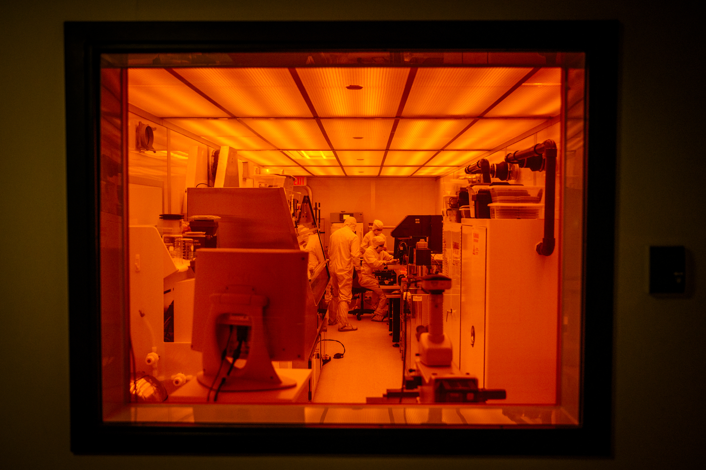 Scientists dressed in full protective gear work in a lab. The photo is bathed in red light.