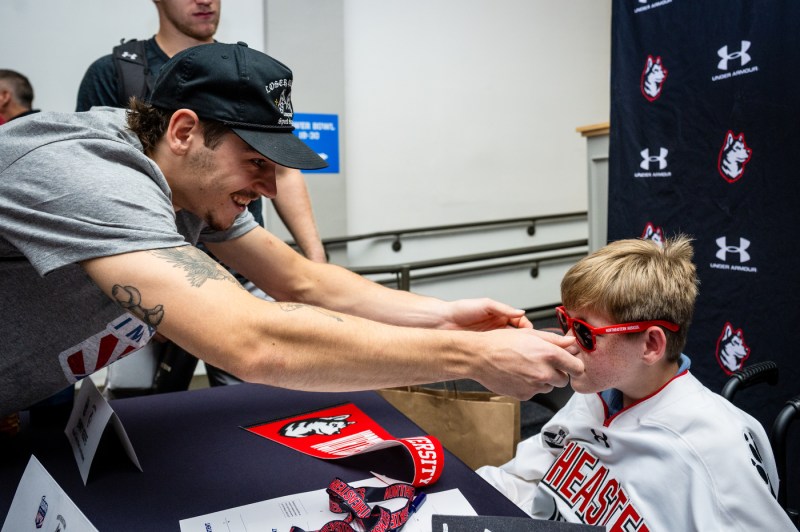 A men's hockey player puts red sunglasses on Mack Welby.
