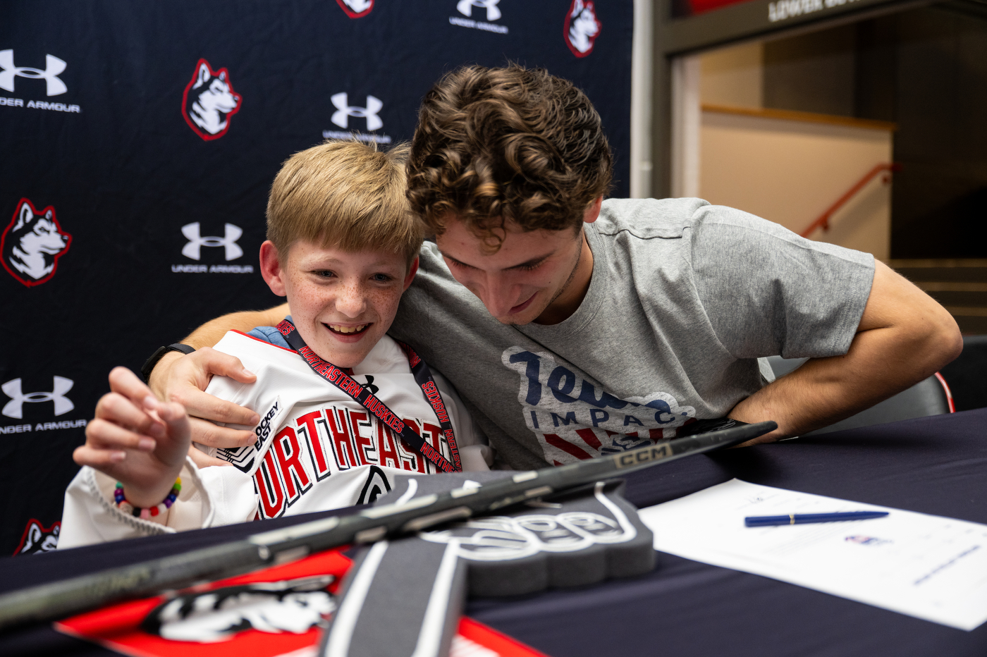 A Northeastern men's hockey team player hugs Mack Welby, who is smiling.