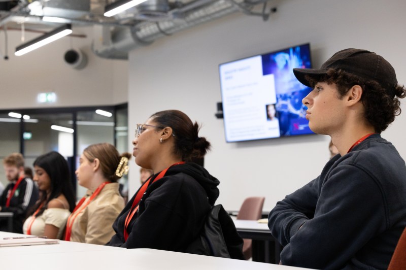 People sit at a long table while listening to a presentation.