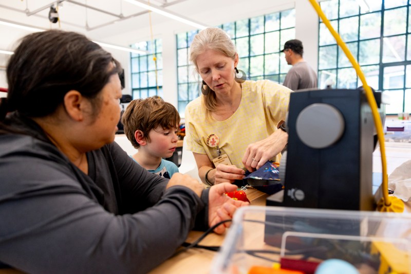 A person shows two other people how to repair a rain jacket with a sewing machine.
