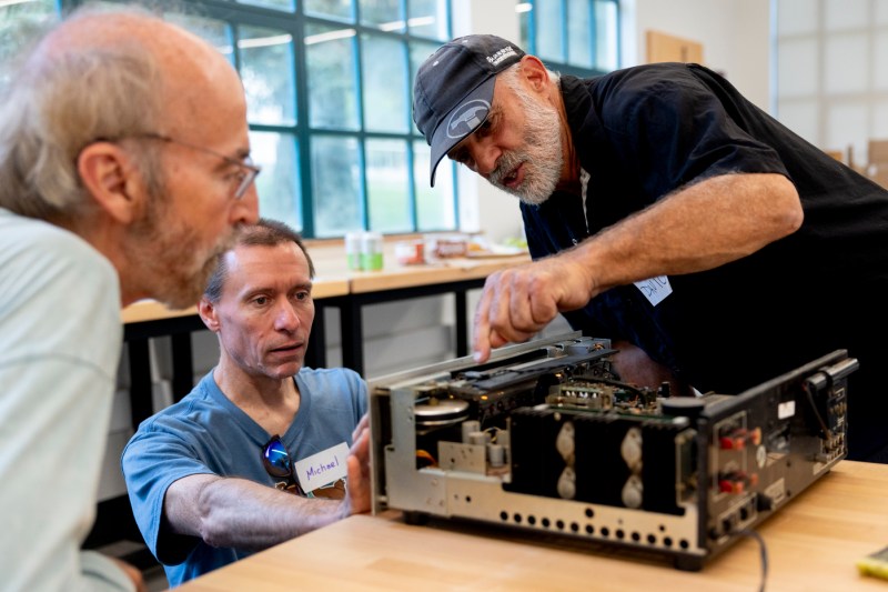 Two people help another person fix a stereo amp. 