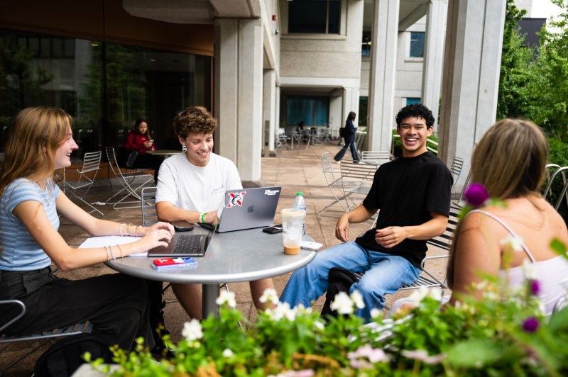 Four students sit at a round table outside of Snell Library.