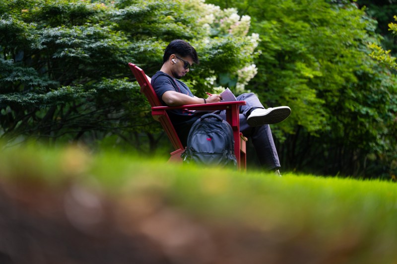 A student sits outside in an Adirondack chair on campus.