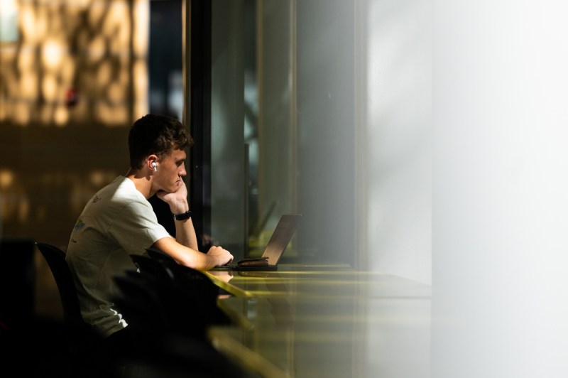 A person sits at a table while working on a laptop.