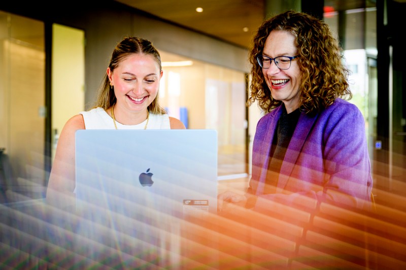 A student works on a computer while a professor looks at the computer.