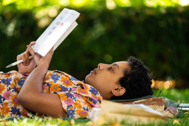 A person lies on their back in the grass while reading a book.