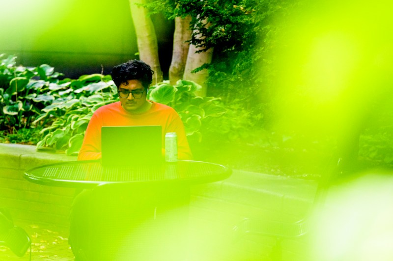 A student sits at a round table outside while working on a laptop.