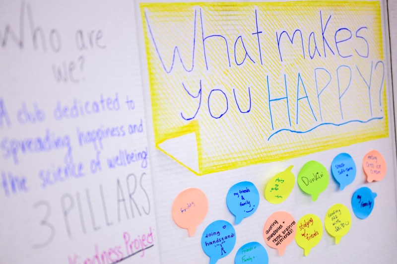 A poster reading “What makes you happy?” is displayed with colorful sticky notes filled with handwritten answers.